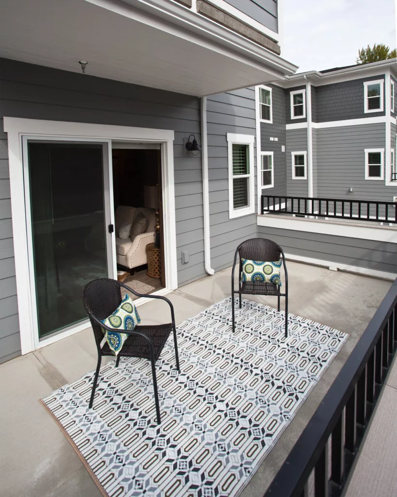 Balcony with two outdoor chairs, rug and sliding glass door behind.