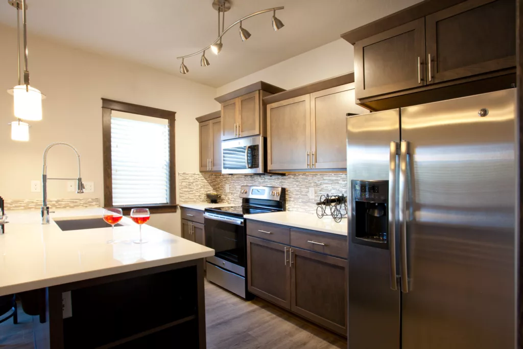 Galley kitchen, stainless steal appliances, brown cabinets, island with white countertops.